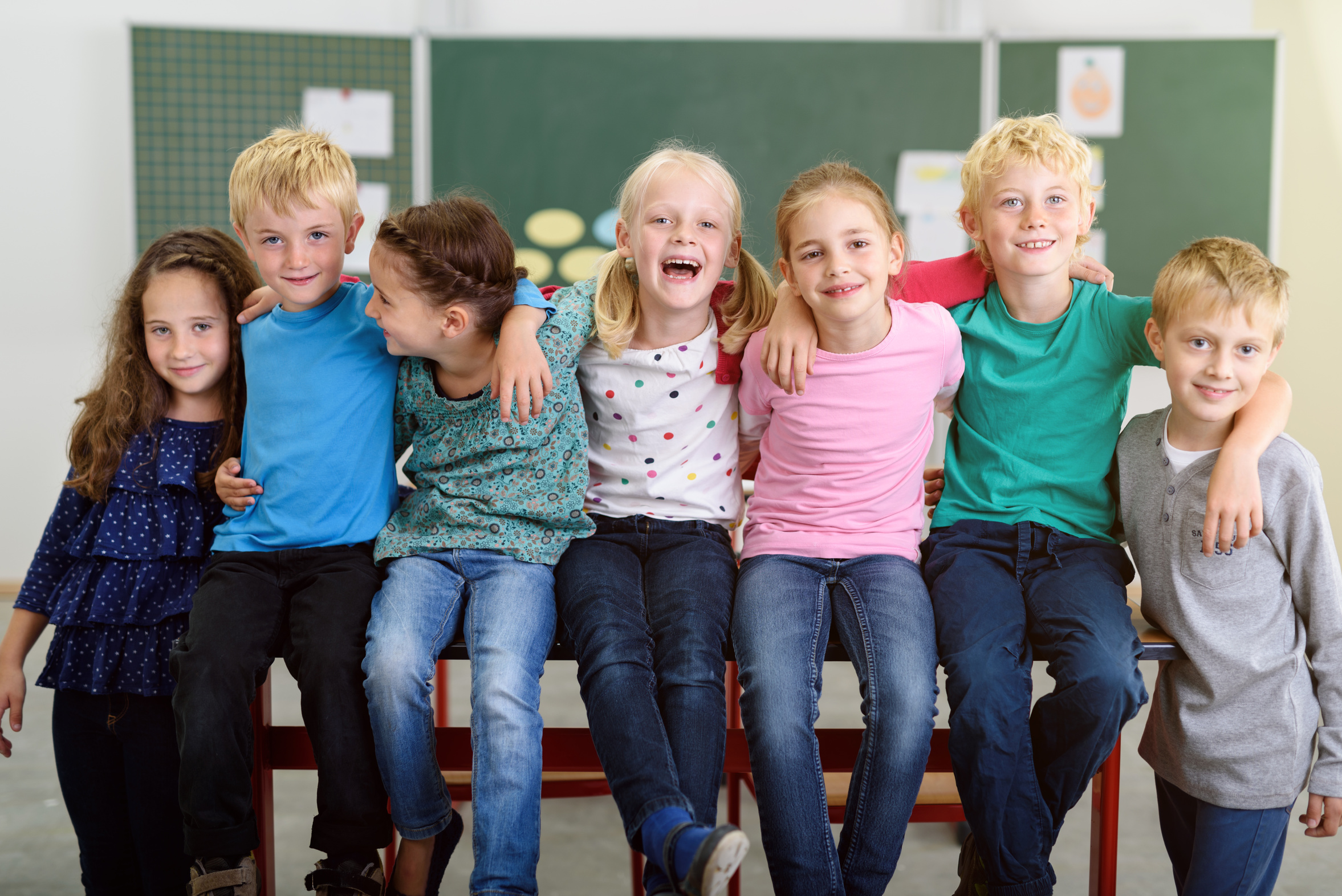 lachende kinder in der grundschule sitzen auf dem tisch